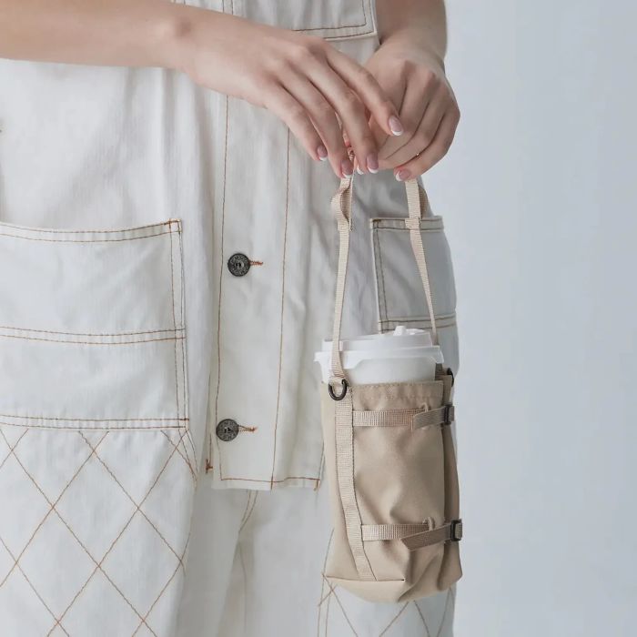 Person carrying a Sand beige Bitplay Waterproof Bottle Carrier 305D CORDURA 210D Nylon Ripstop Pouch with Lanyard Strap on a plain background