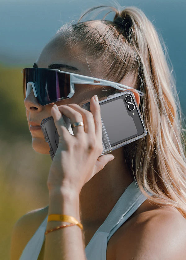 Person wearing futuristic sunglasses with a Person holding a phone with a Clear ITSKINS Hybrid R Clear Hinge Magnetic Case for Samsung Galaxy Z Flip 7 (2025) on a blurred natural background