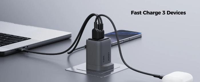 Gray Aukey PA-C5 Comet Mix 3 100W PD Wall Charger with GaN Technology with three ports charging a laptop, phone, and mouse on a gray surface.