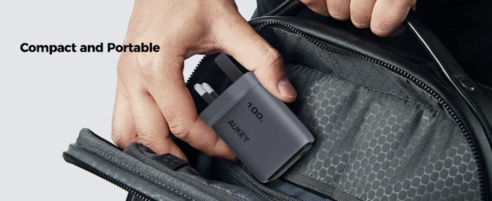 Hand holding a Gray Aukey PA-C5 Comet Mix 3 100W PD Wall Charger with GaN Technology inside an open black bag with 'Compact and Portable' text.