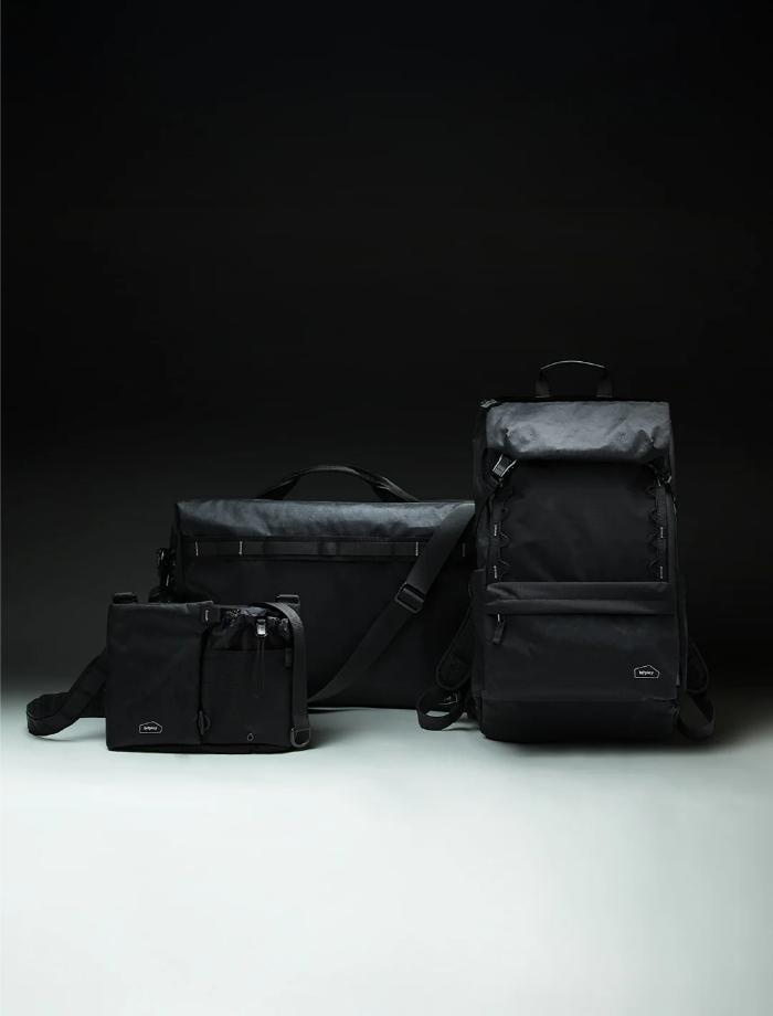 Set of black bags including a backpack, duffel bag, and Bitplay Black Series Sacoche 2L Crossbody Bag/Chest Bag on a dark background