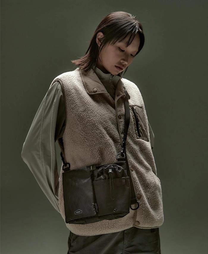 Person wearing a beige vest and carrying a Black Bitplay Black Series Sacoche 2L Crossbody Bag/Chest Bag against a dark background