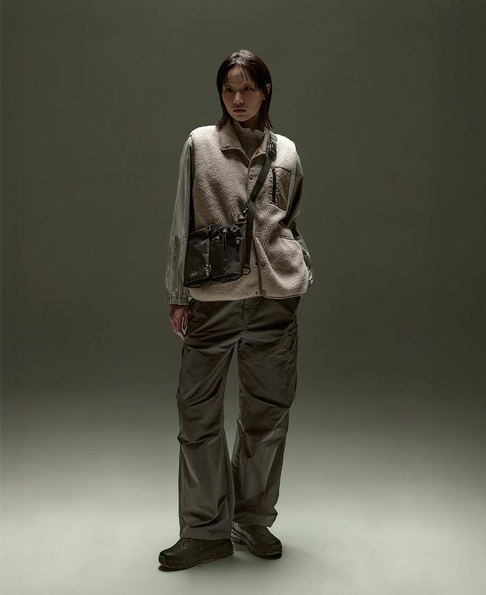 Person wearing a beige vest, gray pants and a Black Bitplay Black Series Sacoche 2L Crossbody Bag/Chest Bag against a plain background