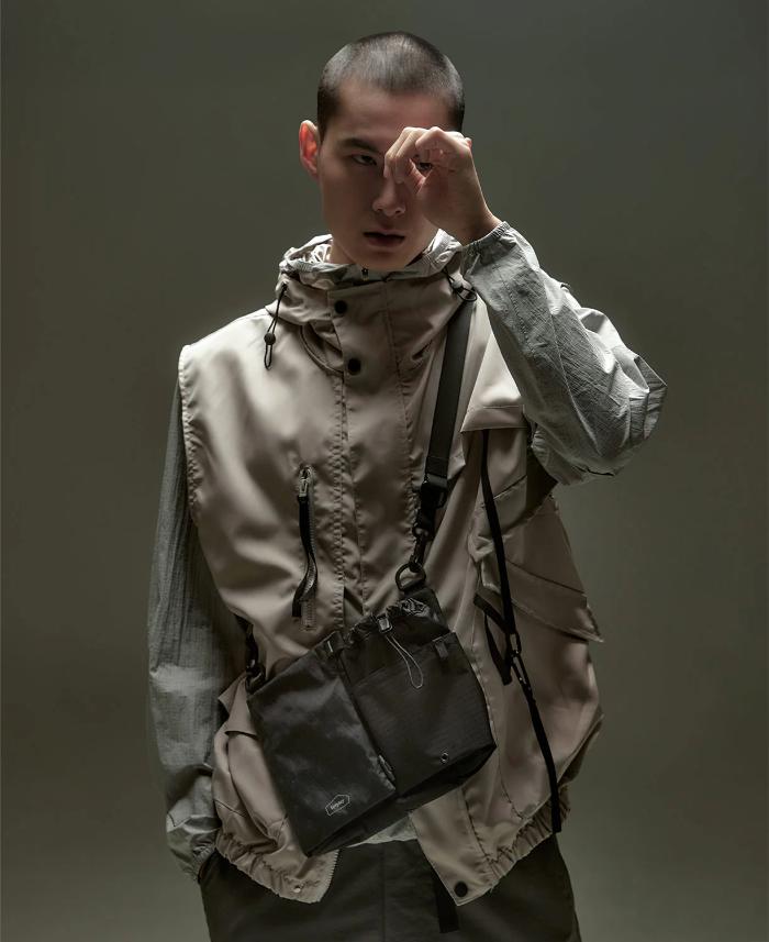 Person wearing a beige jacket with a Black Bitplay Black Series Sacoche 2L Crossbody Bag/Chest Bag on a gray background