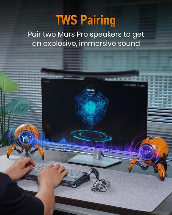 Person using a computer with two GravaStar G1 Pro Mars Pro Wireless Bluetooth 5.0 Speaker (War Damaged Edition) on a desk, featuring TWS pairing text.