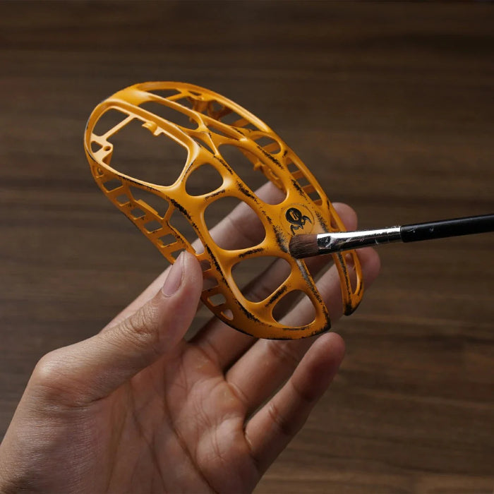 Hand holding a yellow Gravastar Mercury X Wireless Gaming Mouse hollow skeleton with a brush on a wooden background